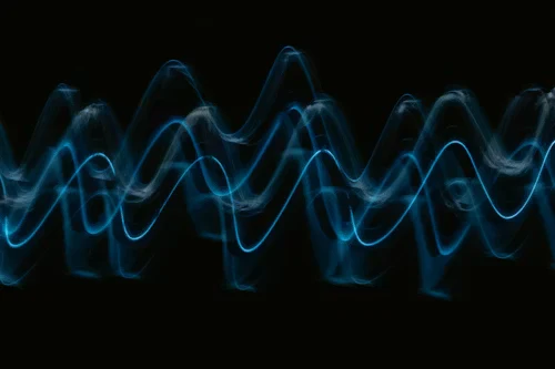 An abstract long-exposure photo of glowing blue sound waves against a black background.